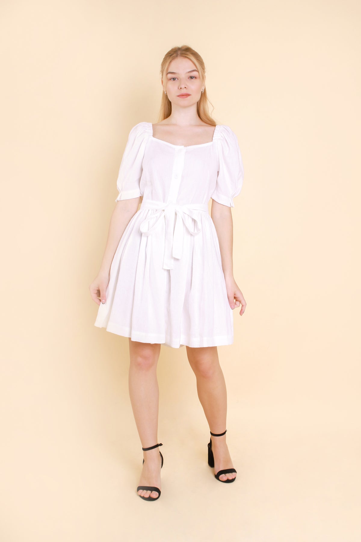 A short and stylish dress is made with linen fabric. The dress features charming puff sleeves and comes with a belt that cinches the waist.